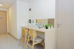 Ein Hotelzimmer mit Schreibtisch aus Holz, zwei Stühlen, einem Spiegel, einer Topfpflanze und einem kleinen Tisch mit Wasserflaschen und einer Kerze.