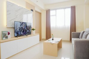 Ein modernes Wohnzimmer mit Flachbildfernseher, einer Couch, einem Couchtisch und einem großen Fenster mit Vorhängen.