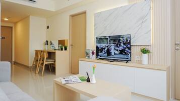 Quarto de hotel moderno com TV de tela plana na parede, escrivaninha de madeira, sofá branco e parede decorativa em mármore.