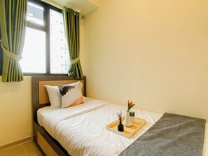 Una cama bien tendida con sábanas blancas, cabecera de madera y una bandeja con un florero y una pequeña planta.