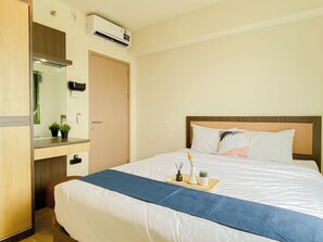 A hotel room with a bed, a bedside table, a mirror, an air conditioning unit, and a door. - Wooden Accents 2Br For 3 Pax At Meikarta District 2 Apartment (Cikarang)