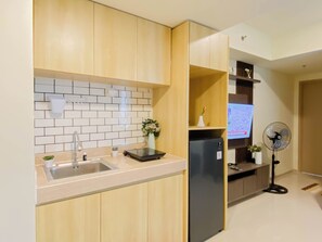 Une cuisine moderne avec des meubles en bois, un pare-feu en carrelage, un évier en acier inoxydable, un réfrigérateur noir et un petit ventilateur.