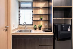 Eine moderne Küche mit integriertem Spülbecken, einem schwarzen Kühlschrank, Holzregalen und zwei Blumentöpfen.