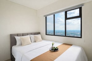 A hotel room with a bed, a window with a city view, and a small table with a plant. - Serene Look 2Br Apartment Meikarta District 2 (Cikarang)