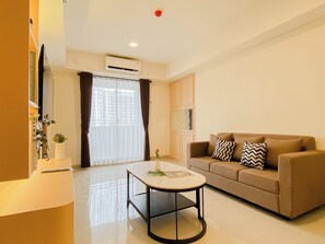 A modern living room with a sofa, a coffee table, and a large window with curtains. - Modern Versatile 3Br At Meikarta District 2 Apartment (Cikarang)