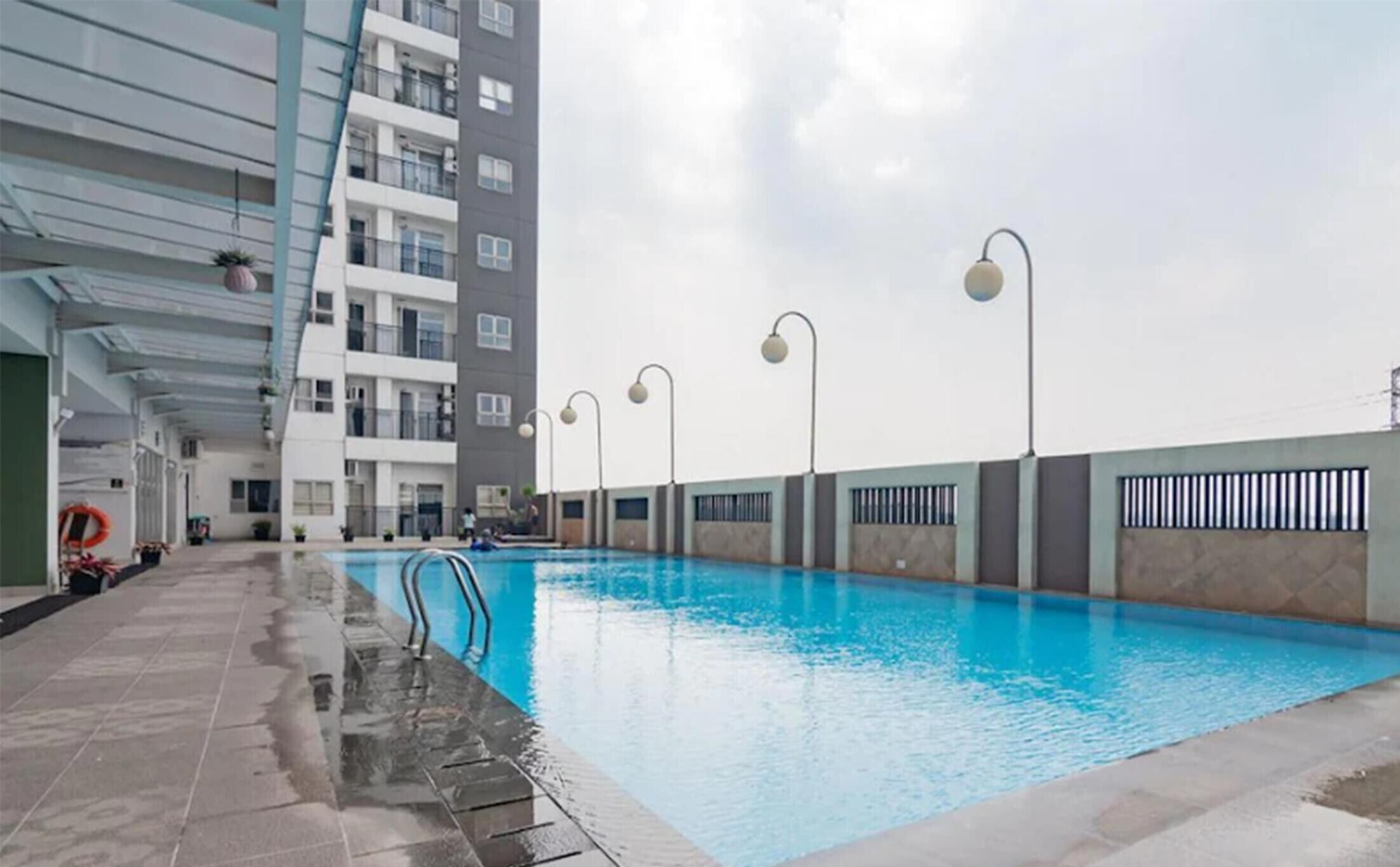 A swimming pool with steps leading into it, surrounded by a modern building with balconies and a covered walkway.