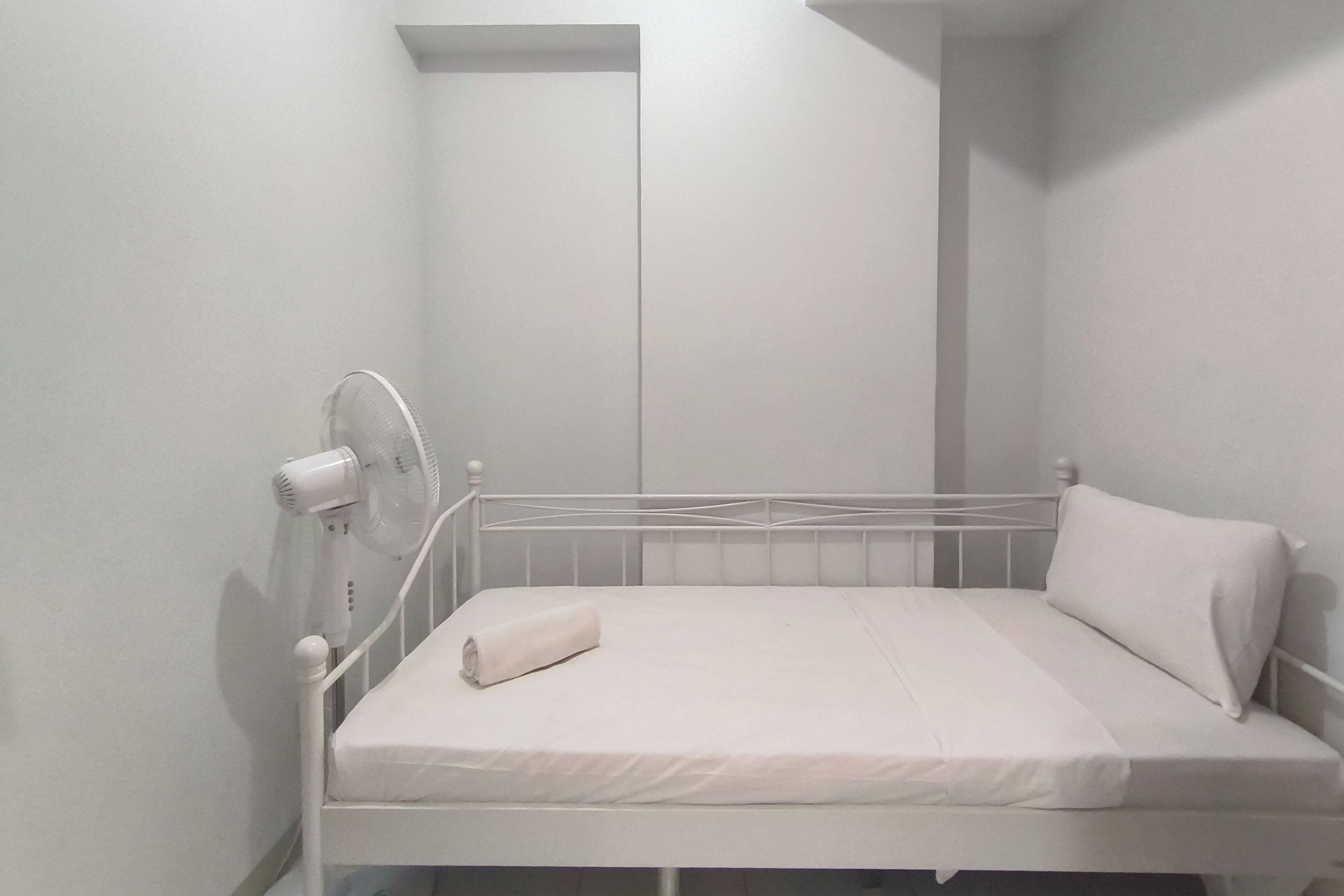 A white metal bed with a white mattress and pillow, a white wall, and a white ceiling.