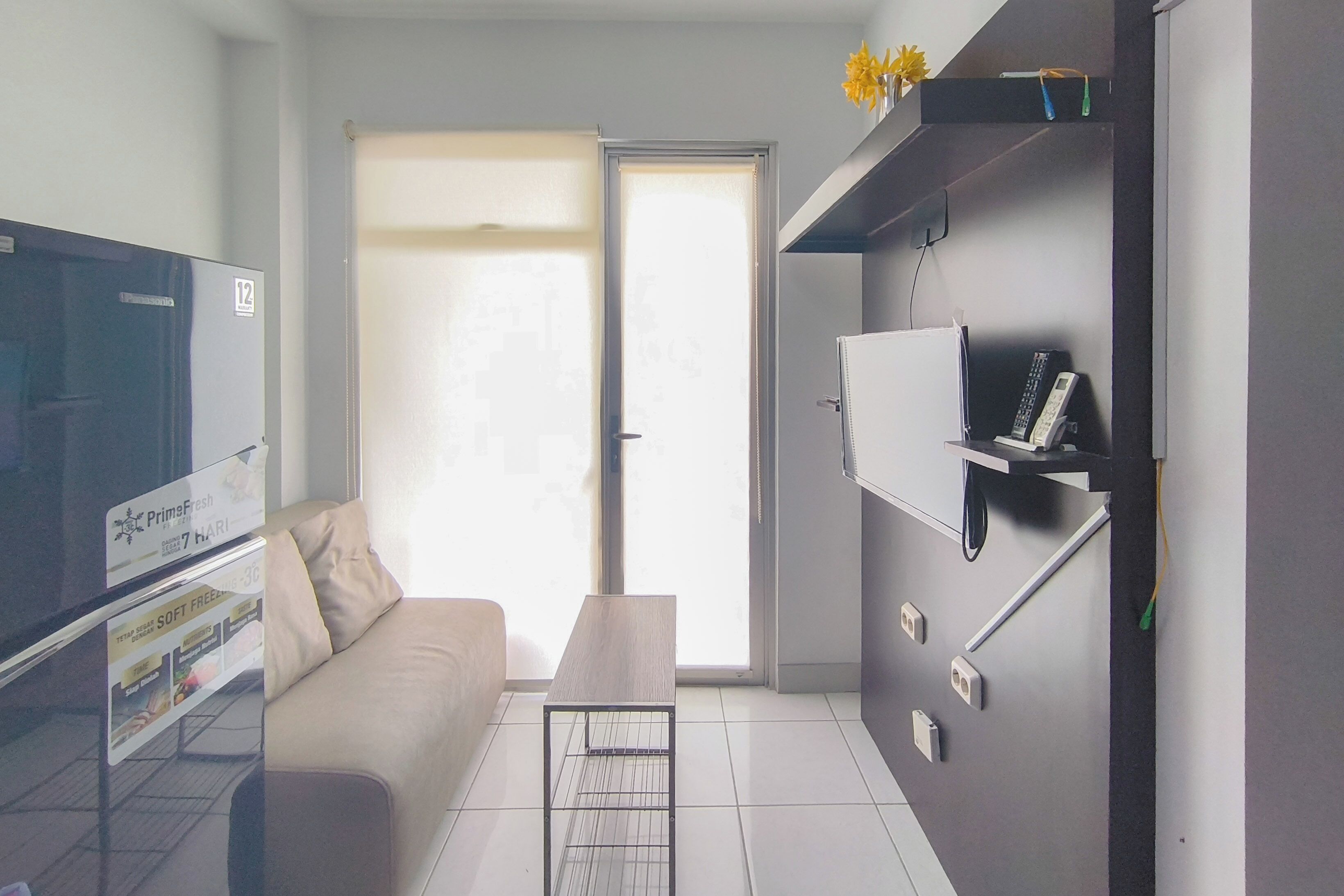 Een moderne woonkamer met een bank, salontafel, flatscreen televisie en een schuifdeur naar een balkon.