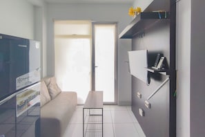 Ein modernes Wohnzimmer mit einer Couch, einem Couchtisch, einem Flachbildfernseher und einer Schiebetür, die auf einen Balkon führt.