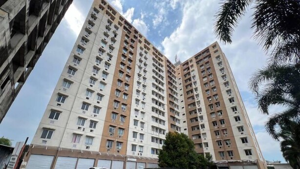 A high-rise residential building with multiple floors, large windows, and a parking area in front.