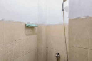 Ein kleiner Duschbereich mit Fliesen, einer Handbrause und einem am Wand montierten Wasserhahn.