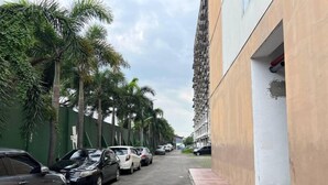 A narrow street lined with parked cars and palm trees, leading to a building with a green exterior and a beige facade. - Restful And Warm Studio At Apartment Menara Rungkut (Surabaya)