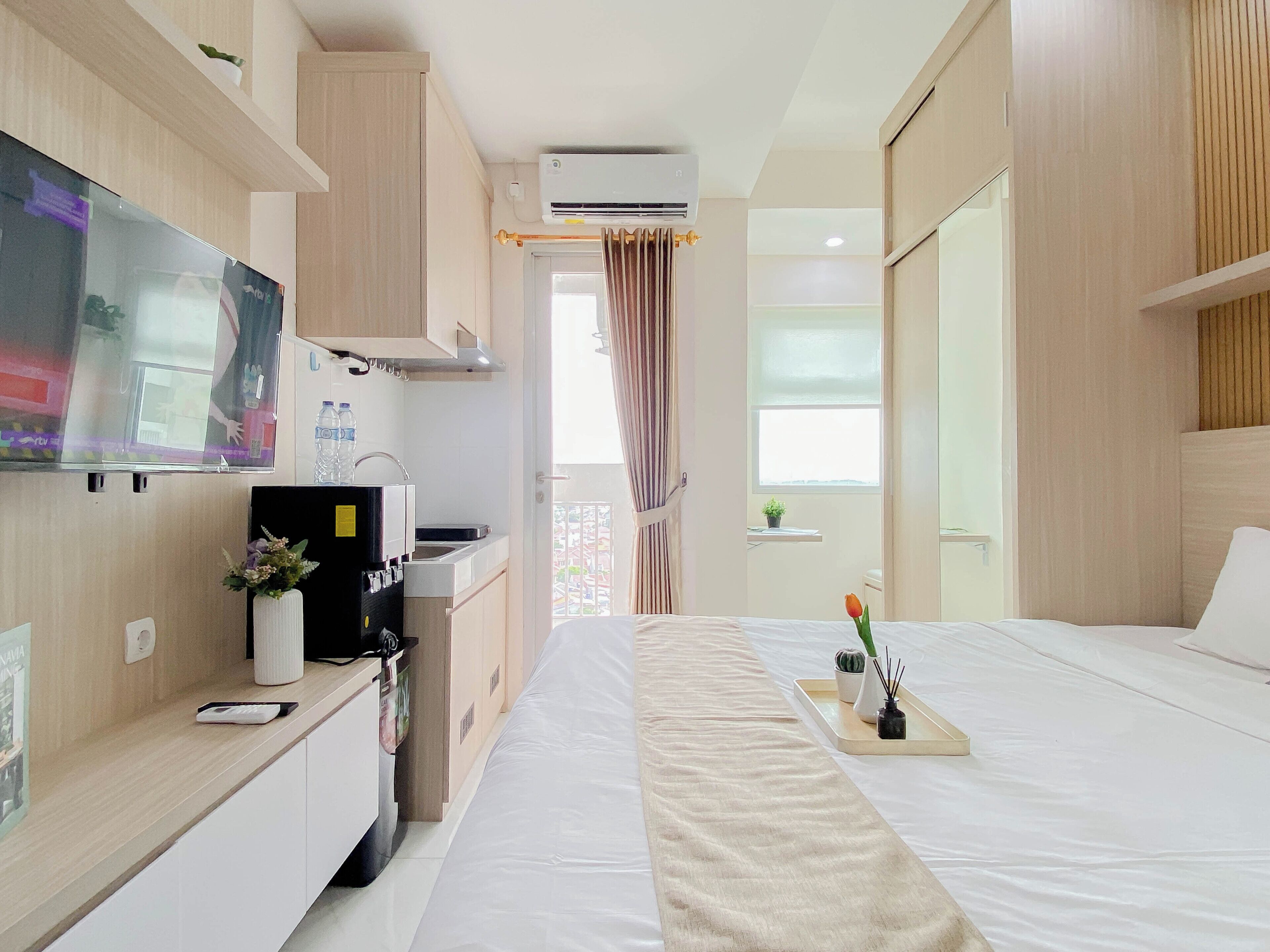 A hotel room with a bed, a TV, a desk with a computer, a mini-fridge, and a window with curtains.