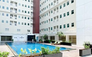 Piscina com espreguiçadeiras e vasos, cercada por um edifício com várias andares e varandas.