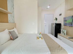 Quarto de hotel com cama, televisão, frigorífico e porta.