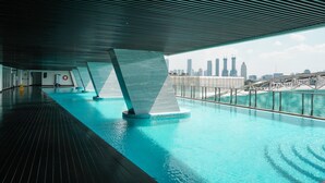 Una piscina interior con vista al horizonte urbano, una terraza de madera y un techo de diseño moderno.