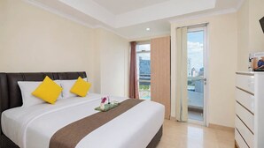 Habitación de hotel con cama, una mesita con bandeja, cómoda y puerta al balcón.