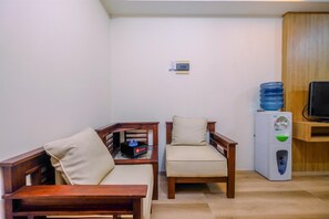 A small room with two wooden chairs, a small table, a water dispenser, and a television on a wooden stand. - Comfy And Minimalist Studio Apartment Metropark Condominium Jababeka (Cikarang)