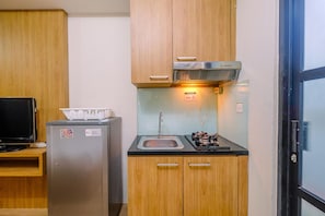 Eine kleine Küchenzeile mit Kühlschrank aus Edelstahl, einer Mikrowelle, einem Spülbecken und Holzschränken.