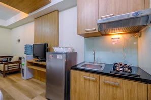 A compact kitchen with wooden cabinets, a stainless steel refrigerator, a built-in stove, and a water dispenser. - Comfy And Minimalist Studio Apartment Metropark Condominium Jababeka (Cikarang)