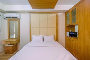 Ein Schlafzimmer mit einem Bett, einem Holzschrank, einem kleinen Schreibtisch mit Spiegel und einer Klimaanlage.