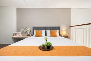 Ein Hotelzimmer mit einem großen Bett, zwei Kissen, einem Nachttisch mit Lampe und einer kleinen Pflanze auf dem Bett.