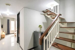 Eine moderne Treppe mit Holzbeschlägen und weißen Geländern, die zu einem Zwischenpodest mit einem schwarzen Gerät und einer Blumenvase führt.