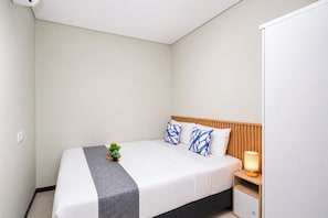 Ein ordentlich bezogenes Bett mit grauer Decke, einem Holzkopfstück und zwei blau gemusterten Kissen.