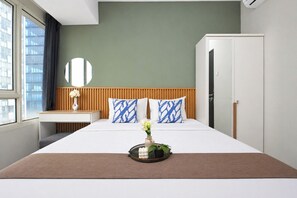 Ein Hotelzimmer mit Bett, Nachttisch, Spiegel, Kleiderschrank und einem Fenster mit Blick auf Gebäude.
