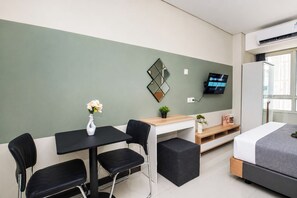 Ein modernes Hotelzimmer mit Bett, Schreibtisch mit Stuhl, Fernseher und einer kleinen Pflanze.