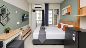 Een hotelkamer met een bed, een bureau, een koelkast, een televisie en een raam met gordijnen.