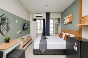 Ein Hotelzimmer mit Bett, Schreibtisch, Kühlschrank, Fernseher und einem Fenster mit Vorhängen.
