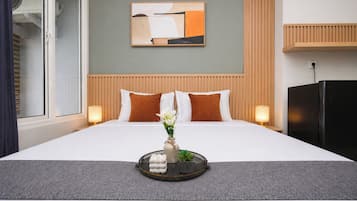 Habitación de hotel con cama, un cuadro abstracto en la pared, cabecera de madera, mesita de noche con lámpara y refrigerador negro.
