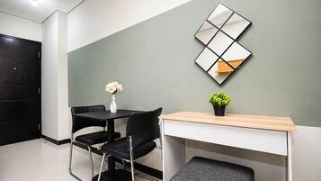 Una habitación moderna con un escritorio, dos sillas, una mesita con un florero y planta, y un elemento decorativo en la pared.