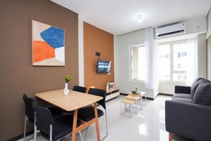 Ein modernes Wohnzimmer mit einer Couch, einem Esstisch mit Stühlen, einem an der Wand montierten Fernseher und einem Fenster mit Vorhängen.
