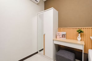 A room with a white wardrobe, a wooden desk with a vase and a book, and a grey bench. - Roomy Urban Living In 3Br At Apartment Nifarro Park (Jakarta)