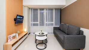 Ett modernt vardagsrum med en grå soffa, ett litet runt bord, en väggmonterad TV och en väggpanel av trä.