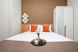 A hotel room with a bed, a bedside table with a tray, a vase with flowers, and a wall-mounted decorative piece. - Roomy Urban Living In 3Br At Apartment Nifarro Park (Jakarta)