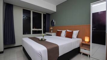 A hotel room with a large bed, a bedside table with a lamp, a window with curtains, and a door.