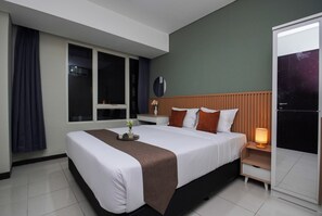 A hotel room with a large bed, a bedside table with a lamp, a window with curtains, and a door. - Roomy And Tidy 3Br At Apartment Nifarro Park (Jakarta)