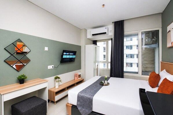 Ein Hotelzimmer mit Bett, Schreibtisch, Fernseher und einem Fenster mit Blick auf Gebäude.