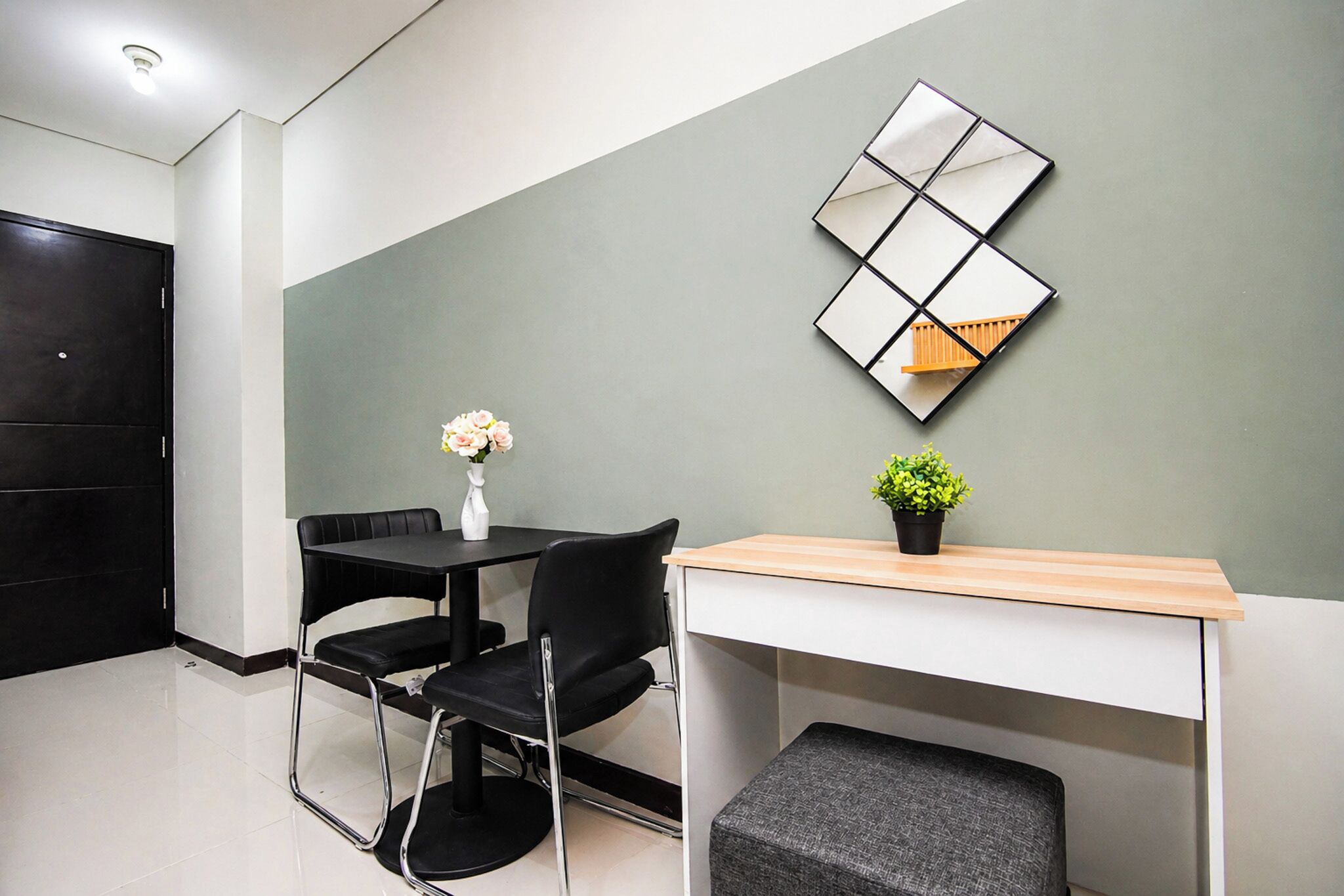 Una habitación moderna con un escritorio, dos sillas, una mesita con un florero y planta, y un elemento decorativo en la pared.