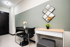 A modern room with a desk, two chairs, a small table with a vase and plant, and a decorative wall piece. - Great Deal Wtih Compact Style Studio At Nifarro Park Apartment (Jakarta)