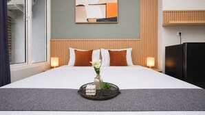 Ein Hotelzimmer mit einem Bett, einem an der Wand hängenden abstrakten Gemälde, einem Holz-Kopfteil, einem Nachttisch mit Lampe und einem schwarzen Kühlschrank.