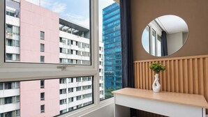 Een kamer met een groot raam, een ronde spiegel, een houten bureau en een kleine plant.