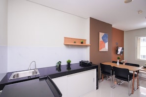 Eine moderne Küche mit schwarzem Tresen, einer Edelstahl-Spüle, einem Holzespeise Tisch mit schwarzen Stühlen und einem kleinen Regal mit Pflanzen.