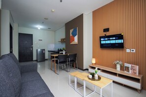 Un salon moderne comprenant un canapé, une table basse, un téléviseur fixé à un mur en bois, un coin repas avec des chaises et une table, et une cuisine en arrière-plan.