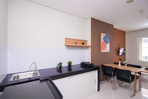 Eine moderne Küche mit schwarzem Tresen, einer Edelstahl-Spüle, einem Holzespeise Tisch mit schwarzen Stühlen und einem kleinen Regal mit Pflanzen.