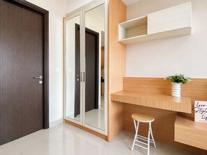 Ein modernes Zimmer mit einer dunkelholzigen Tür, einem Spiegelkleiderschrank, einem Holztisch mit Hocker und einer weißen Vase mit Blumen.