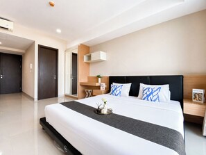 Ein modernes Hotelzimmer mit einem großen Bett, einem Nachttisch, einer Wandablage und einer Tür.